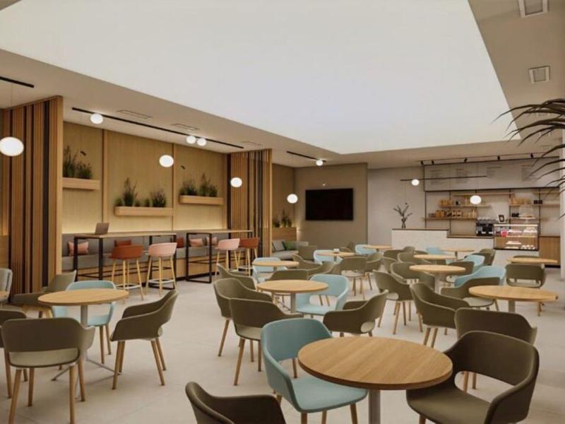 Moderna y luminosa zona de lounge de hotel con mesas, sillas y zona de bar al fondo.