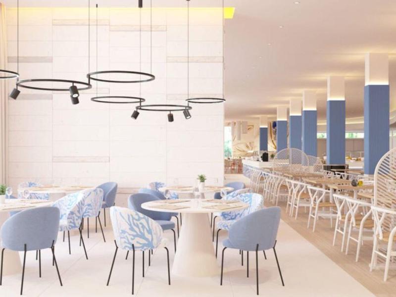 Área de comedor luminosa con sillas azules, mesas blancas y modernas lámparas colgantes.