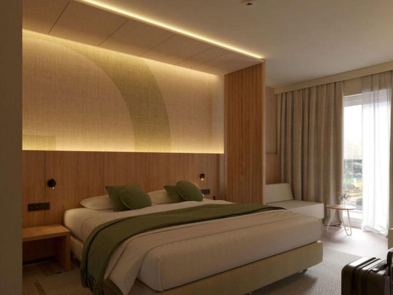 Habitación de hotel moderna con cama grande, ropa de cama verde y blanca y cortinas junto al balcón