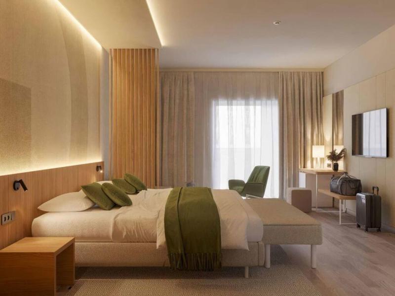 Habitación de hotel moderna con dos camas, acentos verdes y un escritorio frente a una ventana grande.