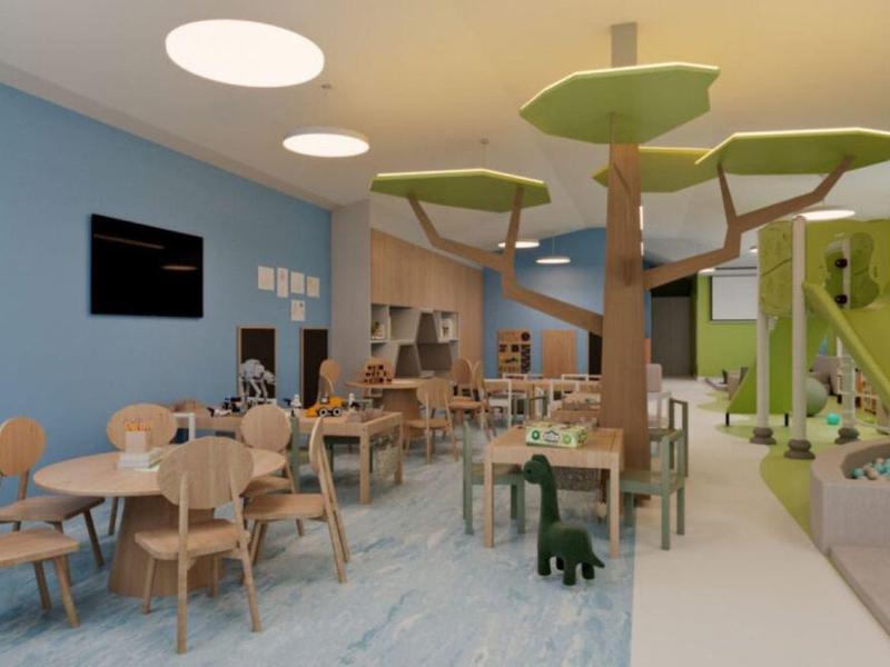 Sala de comedor moderna con sillas de madera, mesas, decoración de árbol y tobogán en área infantil de hotel.