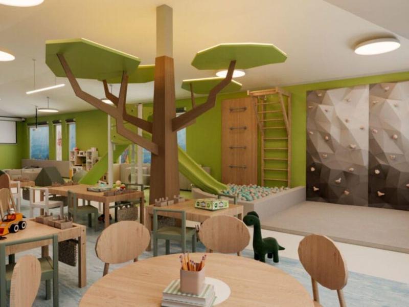 Espacio de aprendizaje para niños con mesas, estructura de árbol y muro de escalada en tonos cálidos.