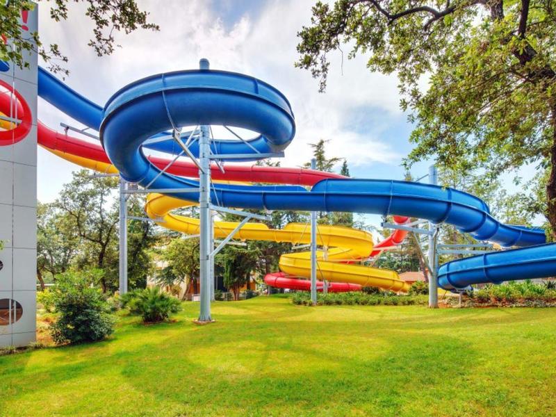 Toboganes de agua coloridos al aire libre rodeados de árboles y césped verde.
