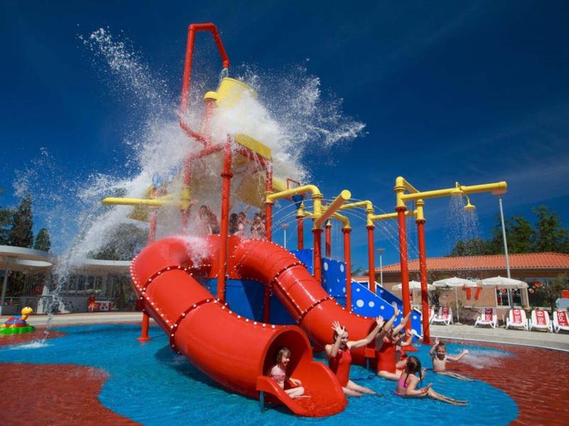 Parque acuático con toboganes tubulares coloridos y niños jugando bajo cielos soleados