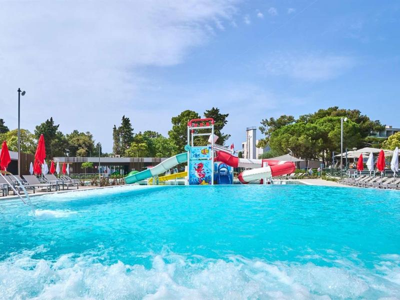 Großer Außenpool mit Wasserrutschen und Liegestühlen bei sonnigem Wetter.