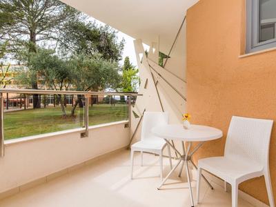 Malý balkon se dvěma bílými židlemi a kulatým stolem s výhledem na zeleň a stromy.