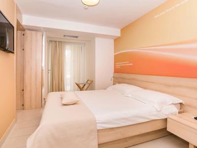 Světle zařízený hotelový pokoj s manželskou postelí, televizí na zdi a skříní.