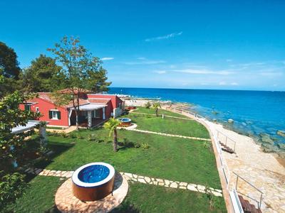 Uitzicht op een vakantiehuis aan zee met groen gazon, terras en heldere blauwe lucht.
