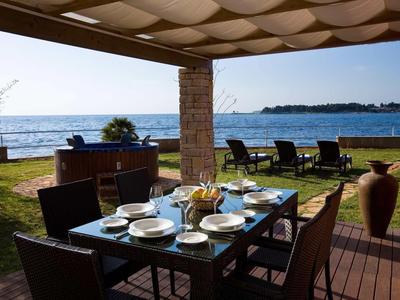 Buiten eetgedeelte met uitzicht op zee, gedekte tafel en ligstoelen onder een pergola.