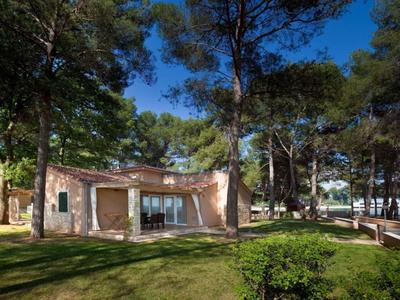 Klein vakantiehuis met terras in een bebost tuin onder een heldere blauwe lucht.