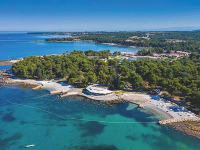 Luchtfoto van een kustlijn met helder water, beboste gebieden en een rond gebouw op het strand.