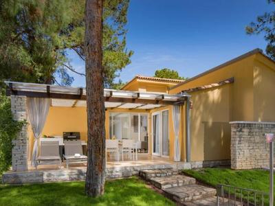 Modern geel vakantiehuis met terras, tuin en zonnige lucht op de achtergrond.