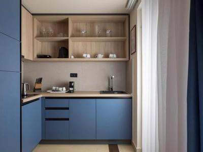 Moderne kitchenette met blauwe kasten, houten blad en open planken in een lichte ruimte.