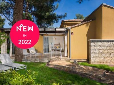 Moderne gele bungalow met terras, tuin en ligstoelen bij zonnig weer