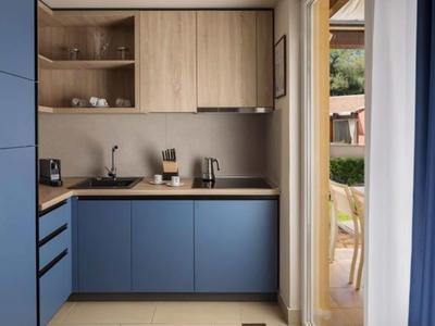 Kleine moderne keuken met blauwe onderkasten en houten bovenkasten naast een deur naar het balkon.