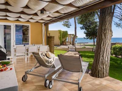 Terrasse mit Liegestühlen und Tisch, Blick auf Meer und Garten in Hotelanlage.