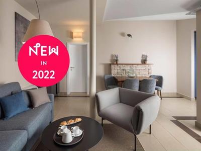 Modern woonkamer met grijze bank, fauteuil en salontafel in een lichte ruimte.