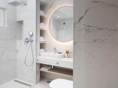 Modernes Badezimmer mit Rundspiegel, Regendusche und beleuchtetem Waschbeckenbereich.