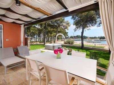 Überdachte Terrasse mit Esstisch und Liegestühlen, Blick auf Meer und Bäume.