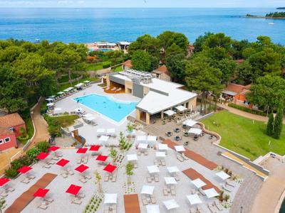 Hotelanlage mit Pool, Liegestühlen und Meerblick in grüner Umgebung.