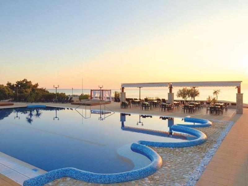 Hotelzwembad bij zonsondergang met ligstoelen en poolbar aan zee.