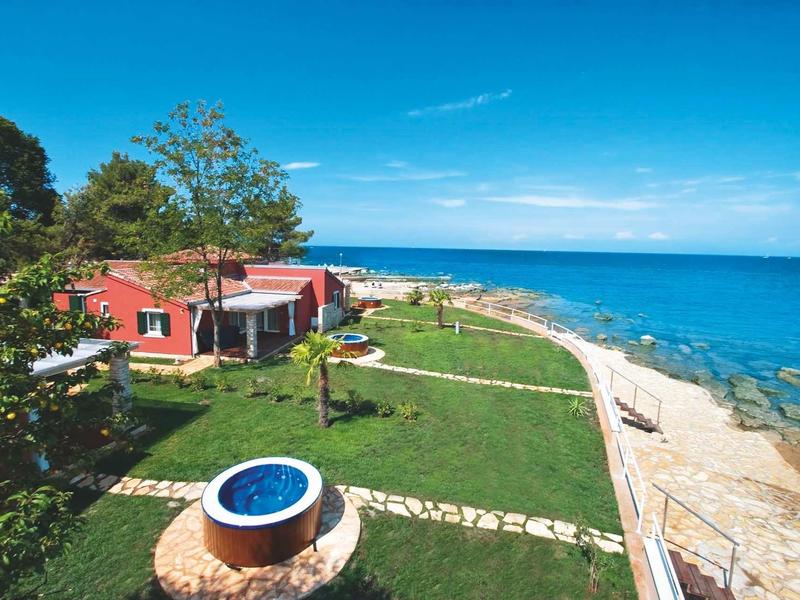 Rood huis aan zee met groen gazon en blauwe lucht langs de kust.