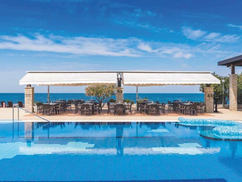 Groot zwembad met zithoek en zeezicht onder een blauwe lucht.