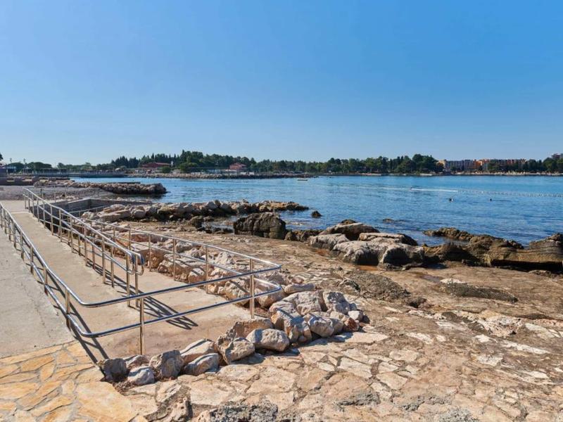 Kustgebied met rotsachtige oever, heldere blauwe lucht en een wandelpad met leuning.