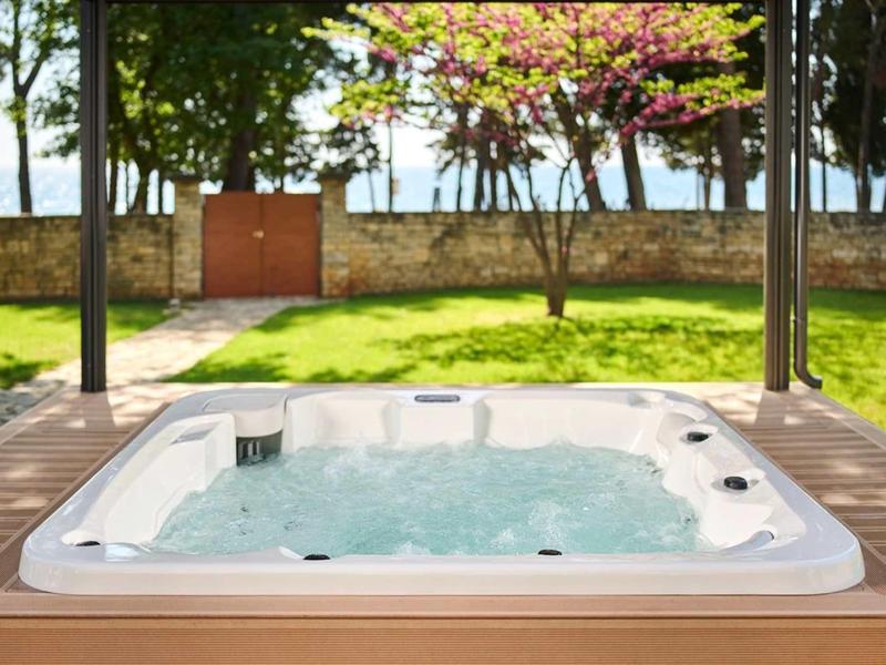 Bubbelbad op een terras met uitzicht op groen gazon en bloeiende bomen