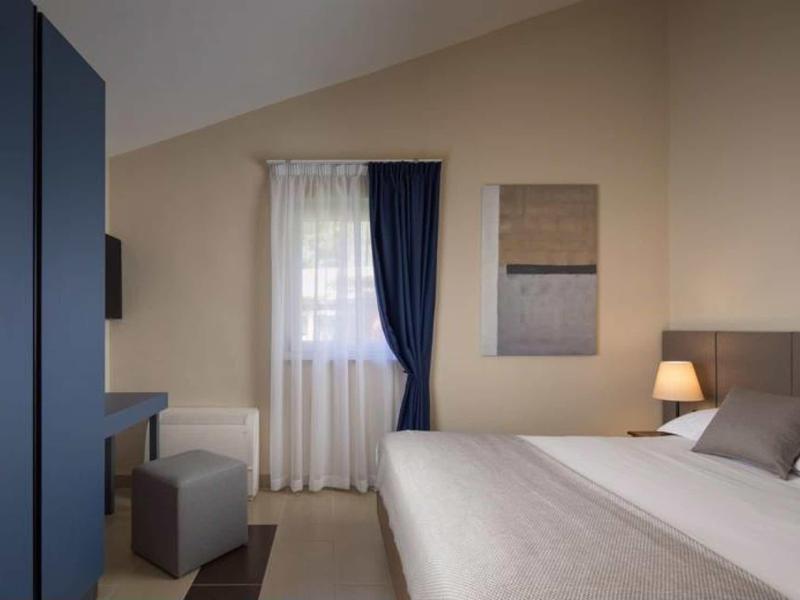 Moderne hotelkamer met tweepersoonsbed, donkerblauwe gordijnen en minimalistische inrichting.