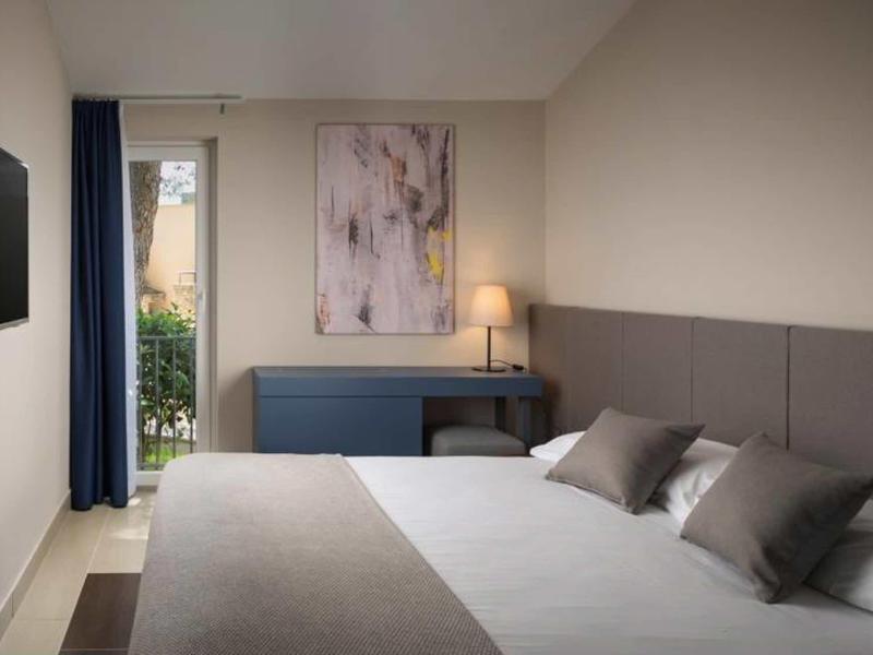 Moderne hotelkamer met tweepersoonsbed, bureau, lamp en zicht op groen buiten door raam.