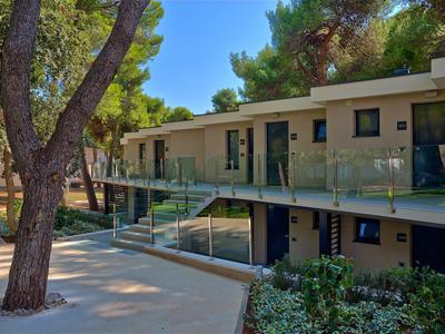 Modern hotelgebouw met glazen leuningen, omgeven door bomen en zonneschijn.