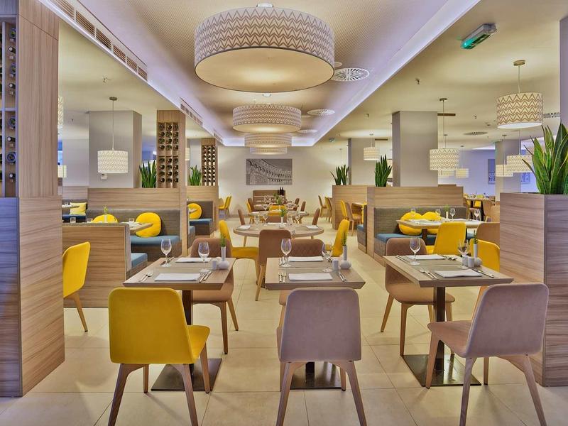 Nowoczesna restauracja z żółtymi krzesłami i drewnianymi stołami, ciepłe oświetlenie, przyjazna atmosfera.