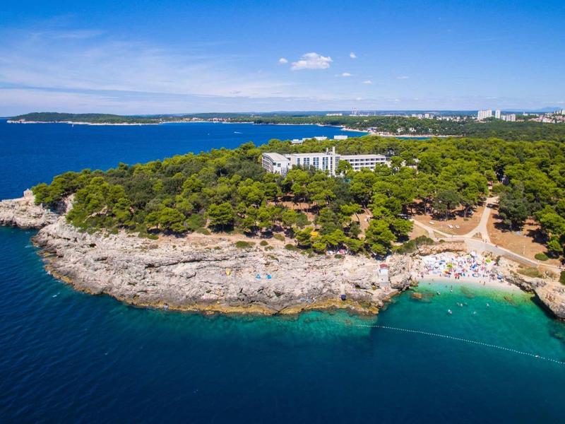 Linia brzegowa z skalistymi klifami, czystą niebieską wodą, zalesionym obszarem i budynkami hotelowymi w tle