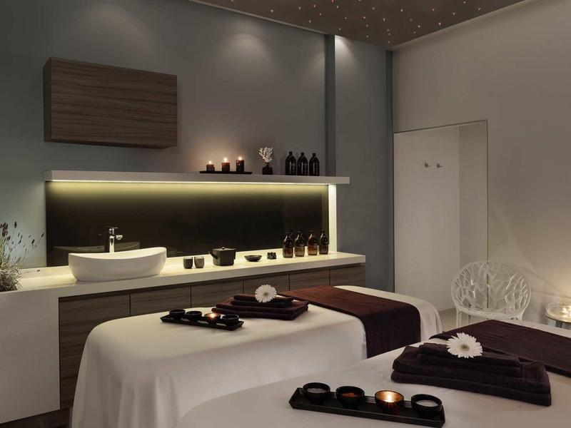 Elegancki pokój zabiegowy z dwoma stołami do masażu, subtelnym oświetleniem i uspokajającą atmosferą.