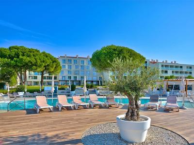 Moderní venkovní bazén hotelu s lehátky, stromy a modrou oblohou.