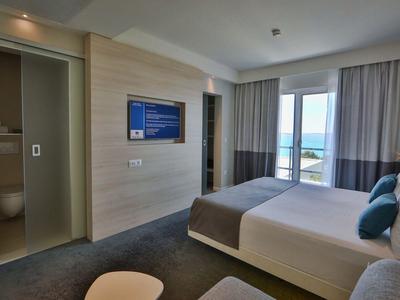 Modernes Hotelzimmer mit Doppelbett, Fernseher, Bad und Meerblick durch große Fenster.