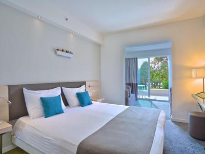 Modernes Hotelzimmer mit Doppelbett, Balkon und Blick auf Grünfläche.