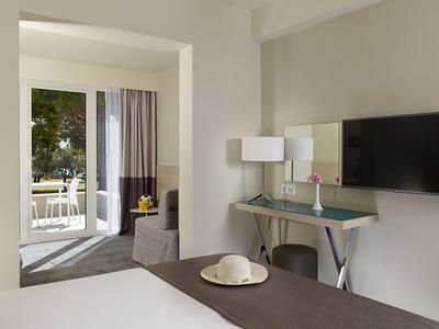 Helles Hotelzimmer mit Bett, Flachbildfernseher, Schreibtisch und Balkon mit Grünblick.