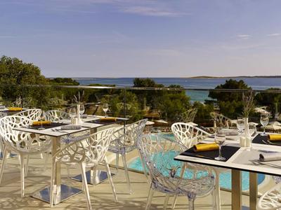 Nowoczesny, elegancki taras z białymi stołami i krzesłami, widok na basen i morze w tle.