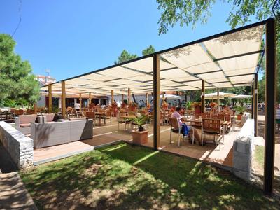 Duży zadaszony taras z miejscami do siedzenia pod czystym niebem i drzewami w tle.