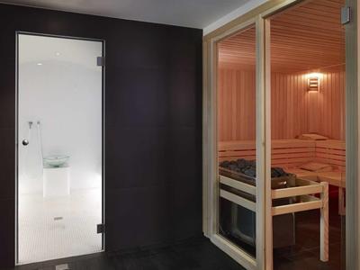 Sauna z drewnianymi ławkami i mlecznymi drzwiami w nowoczesnej strefie spa.