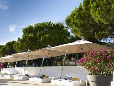 Nowoczesny teren zewnętrzny z białymi parasolami i dużymi donicami przed zielonymi drzewami