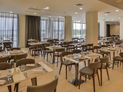 Jasna, nowoczesna restauracja hotelowa z licznymi nakrytymi stołami i beżowymi ścianami.