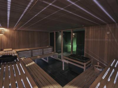 Pomieszczenie sauny z drewnianymi panelami i ławkami, przyciemnione oświetlenie, nowoczesny wygląd.
