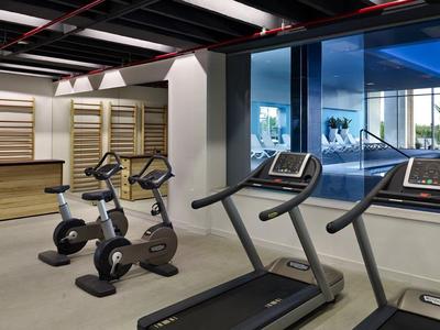 Fitness místnost se dvěma běžeckými pásy a dvěma jízdními koly před velkými okny s výhledem na venkovní prostor.