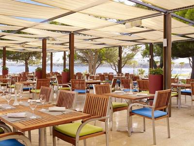 Restauracja na świeżym powietrzu z drewnianymi stołami i krzesłami pod białymi markizami z widokiem na morze.