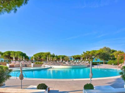 Duży niebieski basen z parasolami i drzewami pod jasnym niebem.