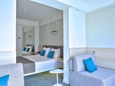 Modern eingerichtetes Hotelzimmer mit Doppelbett, grauen Sesseln und blauen Kissen.