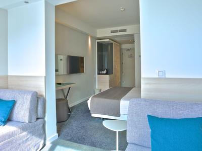 Modernes Hotelzimmer mit Sitzbereich, Bett und heller Farbgestaltung.